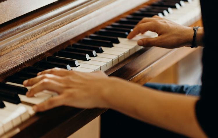 Hands playing a wooden piano - How Much Does Piano Tuning Cost?