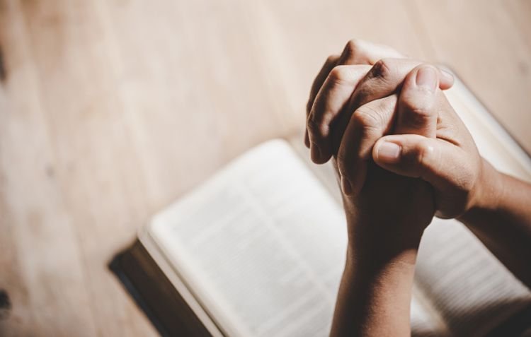 Praying hands over a Bible | How to Avoid a Routine Lifestyle Based on the Bible