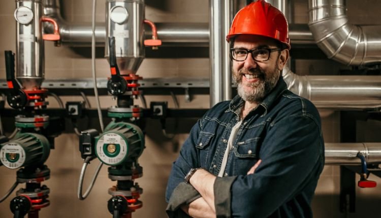 Experienced technician standing confidently in front of pipes.