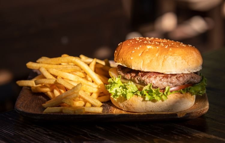 Classic beef burger with fries on a wooden plate.