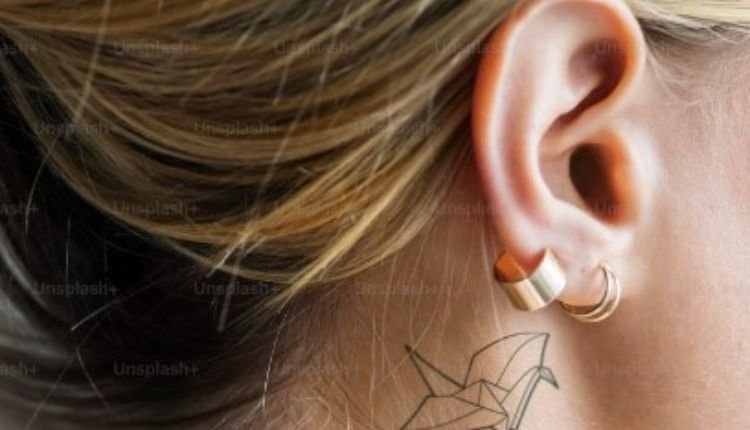 Close-up of an ear with gold earrings and a delicate neck tattoo.