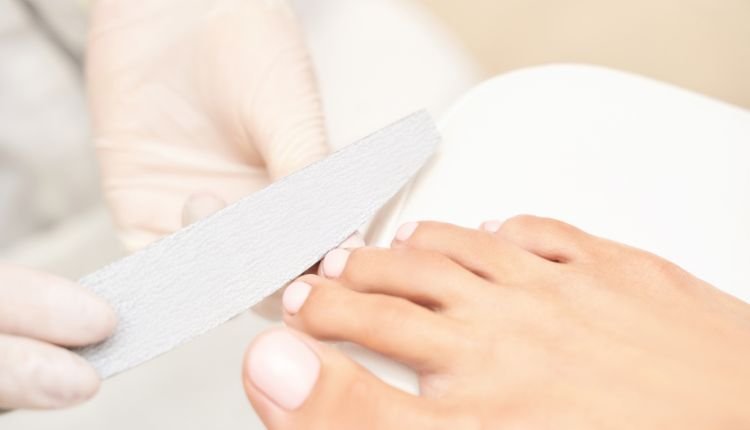 Nail technician filing toenails for a pedicure session.