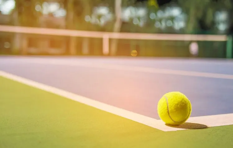 A tennis ball on the court with the net in the background.