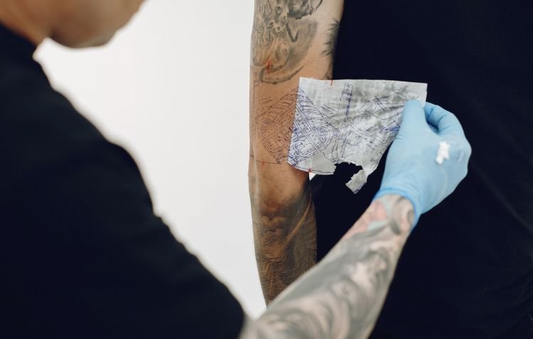 Tattoo artist applying stencil - How Long to Keep Tattoo Wrapped in Cling Film